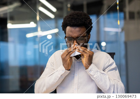 Professional setting depicts individual sneezing due to illnesses like a cold or allergy. Depicts health concerns and workplace well-being. 130069473