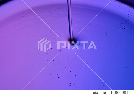 Serum or body cream flows into a petri dish on a purple background. 130069815
