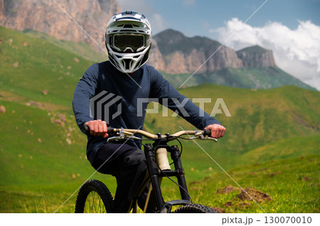 Male athlete cyclist in helmet and protective mask outdoors. MTB rider in mountainous terrain against the backdrop of epic rocks. Male athlete cyclist in helmet and protective mask outdoors. MTB rider in mountainous terrain against the backdrop of epic rocks. 130070010