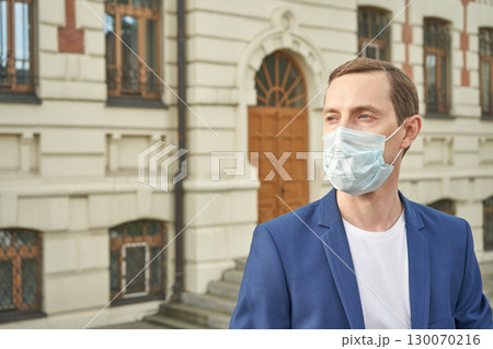 Young caucasian male in blue suit wearing face mask outdoors near historic 130070216