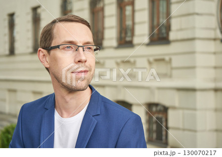 Caucasian male young adult with glasses in blue blazer outdoors near historic 130070217