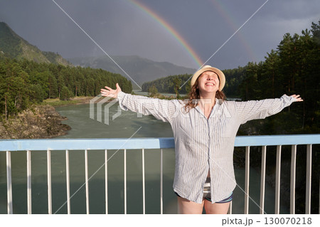 Happy young caucasian female enjoying rainbow on scenic bridge over river 130070218