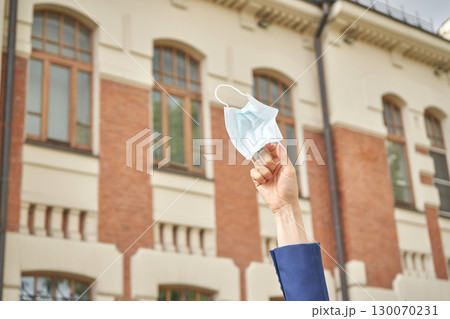 Hand holding medical mask outside brick building symbolizing end of pandemic 130070231