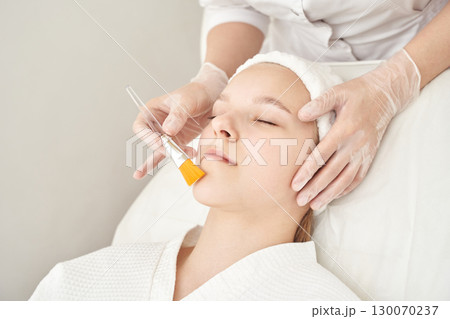 Young caucasian female receiving facial treatment at spa by gloved professional 130070237