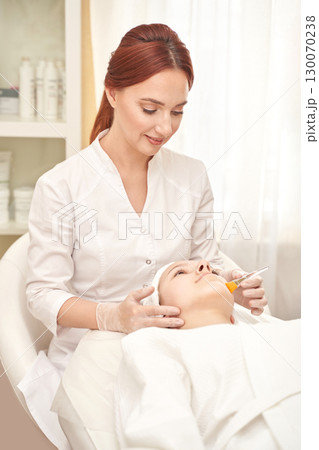 Female aesthetician performing facial treatment on female client in spa setting Female aesthetician performing facial treatment on female client in spa setting 130070238