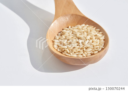 Raw brown rice in wooden spoon on white background with shadow play highlighting 130070244