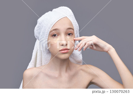 Young caucasian female with eye patches and towel wrapped head on grey Young caucasian female with eye patches and towel wrapped head on grey 130070263