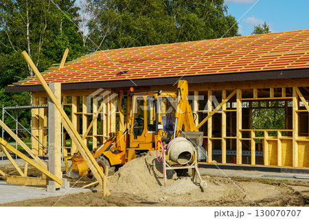 Excavator and cement mixer at wooden frame house construction site with roof beams 130070707