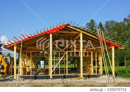 New modern wooden house under construction with visible frame, roof beams, and scaffolding support New modern wooden house under construction with visible frame, roof beams, and scaffolding support 130070732