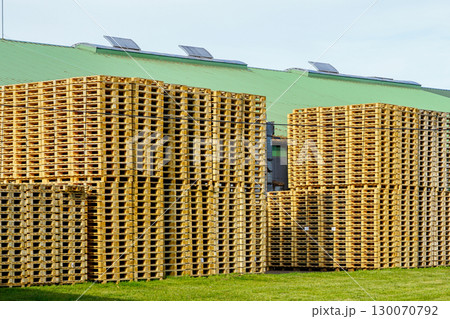 Large stacks of new wooden pallets stored outside an industrial warehouse with green roof Large stacks of new wooden pallets stored outside an industrial warehouse with green roof 130070792