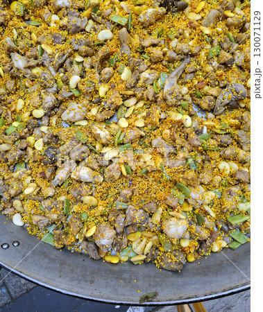 A giant frying pan is sizzling with a colorful mix of rice, tender meat, and fresh vegetables. Aromatic spices create a tempting dish, reflecting local culinary traditions during a sunny day. A giant frying pan is sizzling with a colorful mix of rice, tender meat, and fresh vegetables. Aromatic spices create a tempting dish, reflecting local culinary traditions during a sunny day. 130071129
