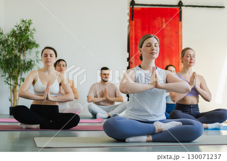 Yoga mindfulness meditation. Group of sporty people doing exercise in studio for class for yoga wellness mindfulness meditation. Men women practicing yoga sitting in lotus pose meditating relaxing 130071237