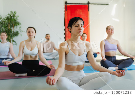 Yoga mindfulness meditation. Group of sporty people doing exercise in studio for class for yoga wellness mindfulness meditation. Men women practicing yoga sitting in lotus pose meditating relaxing 130071238