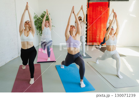 Yoga class Pilates workout. Group of sporty people doing exercise in studio class for yoga wellness mindfulness meditation. Personal trainer men women practicing yoga in gym training stretching indoor Yoga class Pilates workout. Group of sporty people doing exercise in studio class for yoga wellness mindfulness meditation. Personal trainer men women practicing yoga in gym training stretching indoor 130071239