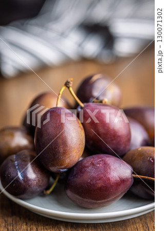 Ripe plums on plate  on wooden table. 130071302