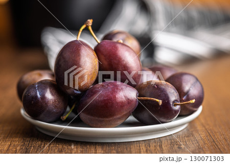 Ripe plums on plate  on wooden table. 130071303
