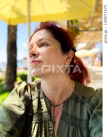 A woman sitting at a cafe terrace under a yellow umbrella. Relaxation, lifestyle, and personal moment outdoors. 130071475