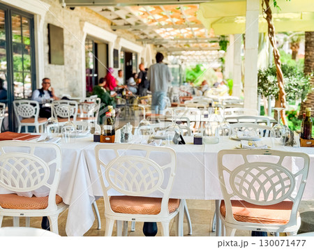 Tables set at an outdoor restaurant with guests in the background. Hospitality, leisure, and summer dining experience. 130071477