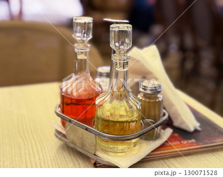 Glass bottles with oil, vinegar and spices on a cafe table. Culinary tradition, Mediterranean lifestyle and casual dining culture indoors. Glass bottles with oil, vinegar and spices on a cafe table. Culinary tradition, Mediterranean lifestyle and casual dining culture indoors. 130071528