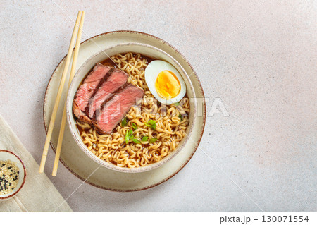 Ramen or asian style noodles soup with beef, egg and green onions in bowl on light beige background top view, space for text 130071554