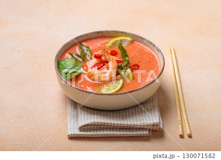 Traditional Thai soup tom yum soup with shrimp, lime, and herbs in bowl with chopsticks on light beige background Traditional Thai soup tom yum soup with shrimp, lime, and herbs in bowl with chopsticks on light beige background 130071582