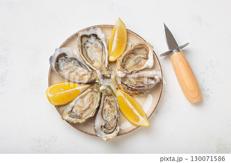 Fresh oysters with lemon wedges and oyster knife on plate top view 130071586