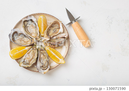 Fresh oysters with lemon wedges and oyster knife on plate top view, space for text Fresh oysters with lemon wedges and oyster knife on plate top view, space for text 130071590