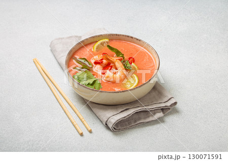 Traditional Thai soup tom yum soup with shrimp, lime, and herbs in bowl with chopsticks on light grey background 130071591