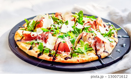 Italian Flatbread With Prosciutto, Arugula, Parmesan And Balsamic Glaze On Black Plate. Concept Of Italian Casual Dining, Summer Pizzas, Artisan Food Culture, And Contemporary Menu Visuals 130071612