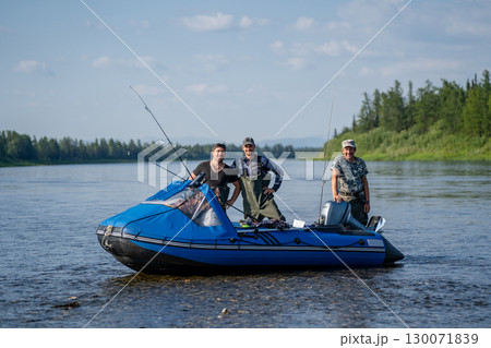 Three happy fishermen in a boat with spinning rods on a river near a forest 130071839