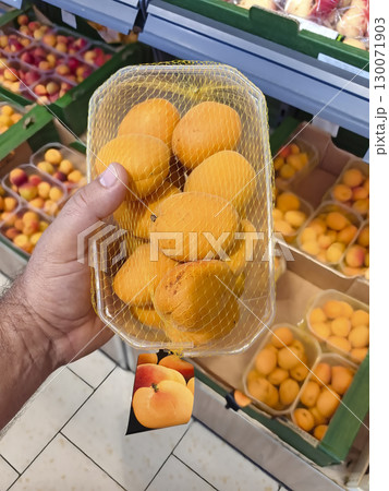 Hand holding fresh yellow apricots in a market basket during summer shopping Hand holding fresh yellow apricots in a market basket during summer shopping 130071903