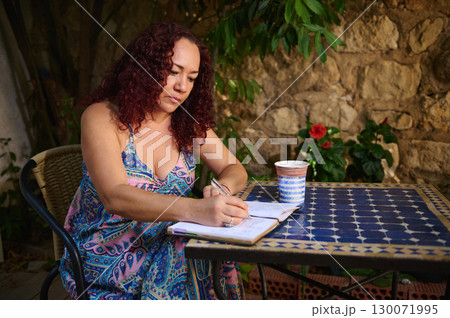 Woman Writing in Journal at Scenic Outdoor Table with Coffee Mug 130071995