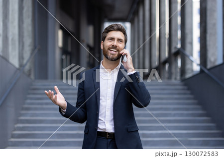 Business professional in a suit talking on a smartphone, exuding confidence outdoors in an urban setting. 130072583