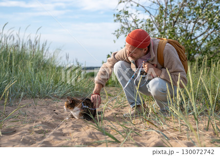 Thoughtful man soothing cat before beach adventure. Cautious pet uncomfortable in strange territory Thoughtful man soothing cat before beach adventure. Cautious pet uncomfortable in strange territory 130072742