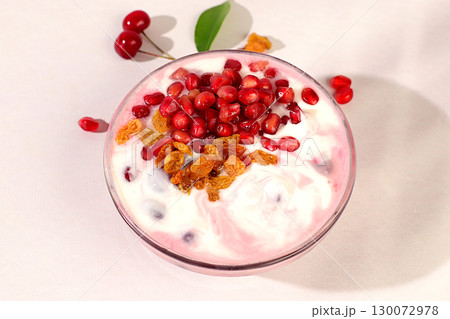 Bowl of pomegranate yogurt with pomegranate pieces, raisins and fresh cow cream for healthy eating on light table. Healthy breakfast with ingredients, kitchen background, Natural nutrition concept. Bowl of pomegranate yogurt with pomegranate pieces, raisins and fresh cow cream for healthy eating on light table. Healthy breakfast with ingredients, kitchen background, Natural nutrition concept. 130072978