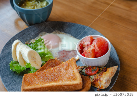 トーストや目玉焼き、バナナやトマト、ピザを盛り付けた洋風朝食プレート 130073019