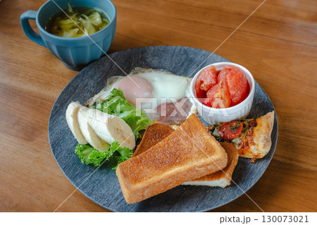 トーストや目玉焼き、バナナやトマト、ピザを盛り付けた洋風朝食プレート トーストや目玉焼き、バナナやトマト、ピザを盛り付けた洋風朝食プレート 130073021