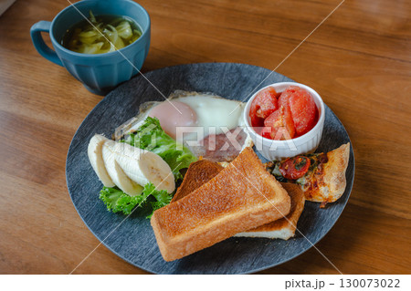トーストや目玉焼き、バナナやトマト、ピザを盛り付けた洋風朝食プレート 130073022