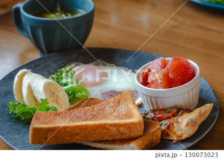 トーストや目玉焼き、バナナやトマト、ピザを盛り付けた洋風朝食プレート 130073023