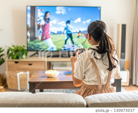 無関心な家族の前で大画面のテレビで一人で熱心にオンラインテレビゲームをする女子中学生 130073037