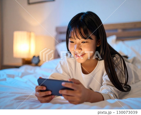 夜にベットでスマートフォンでゲームをする女子中学生 130073039