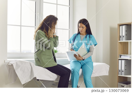 Female patient sitting in the doctor's office with nurse in medical clinic suffering from headache. 130073069