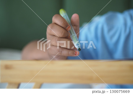 Child holding a pen while drawing on a wooden table Child holding a pen while drawing on a wooden table 130075669