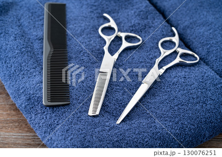 青いタオルの上に置いた散髪用のはさみとすきばさみと櫛のセット 130076251
