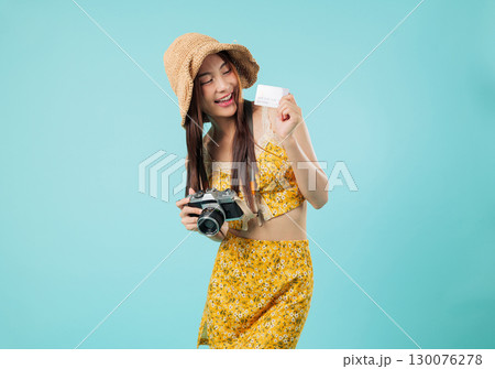 Happy asian woman, credit card, travel camera in hand, she holds bank card for online payment, floral outfit and hat ready to make another payment, enjoying vacation, isolated studio blue background Happy asian woman, credit card, travel camera in hand, she holds bank card for online payment, floral outfit and hat ready to make another payment, enjoying vacation, isolated studio blue background 130076278