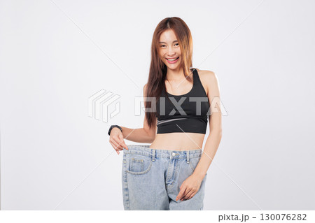 Weight reduction left her jeans oversized, showing off her slim body. She proudly shares her weight journey and inspires others to begin theirs. isolated studio white background 130076282