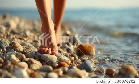 Barefoot woman walking on pebble beach under clear blue sky by the sea 130076802