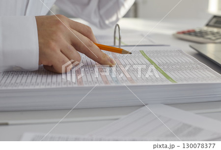 Business accountant holding pencil and working with paper balance sheets on table Business accountant holding pencil and working with paper balance sheets on table 130078377