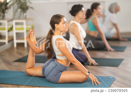 Group of women practicing yoga, working out doing version of Eka Pada Hasta Marjariasana in studio Group of women practicing yoga, working out doing version of Eka Pada Hasta Marjariasana in studio 130078505
