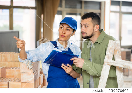 Man architect and woman builder discussing project documentation Man architect and woman builder discussing project documentation 130078605